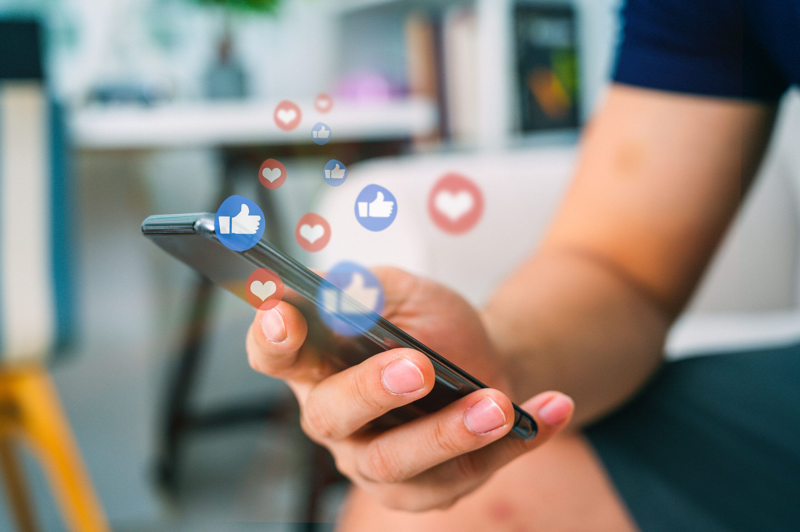 Eine Hand hält ein Smartphone. Mehrere Like-Buttons schweben durch die Luft.